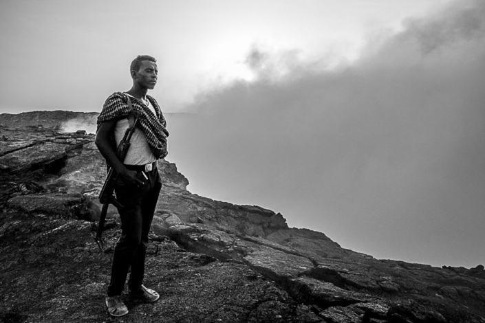 Image noir et blanc d'un homme armé au bord du volcan Erta Ale