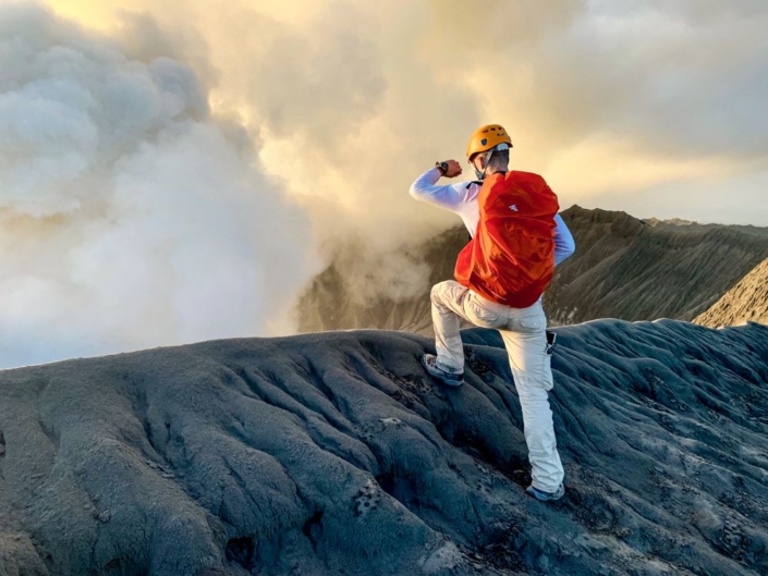 Un alpiniste regarde au fond d'un cratère qui fume