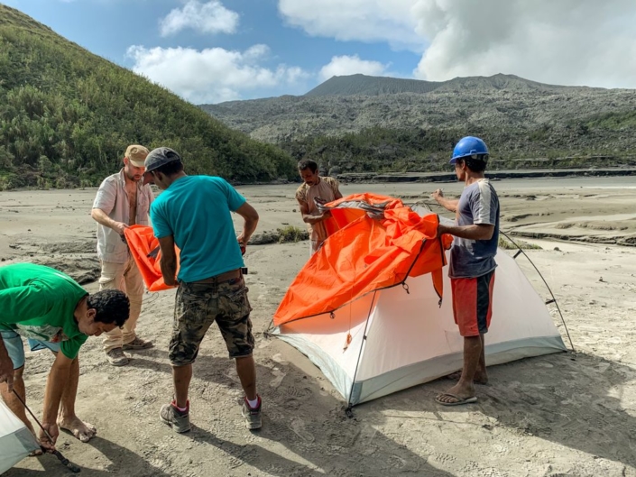Cinq hommes démontent un tente dans la caldeira d'un volcan
