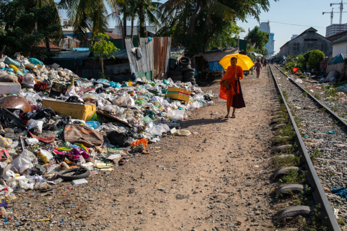 Photographie d'un moine passant devant un tas d'ordure le long d'une voie ferrée