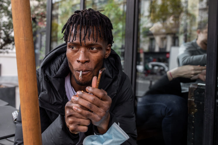 Portrait journalistique d'un migrant allumant une cigarette.