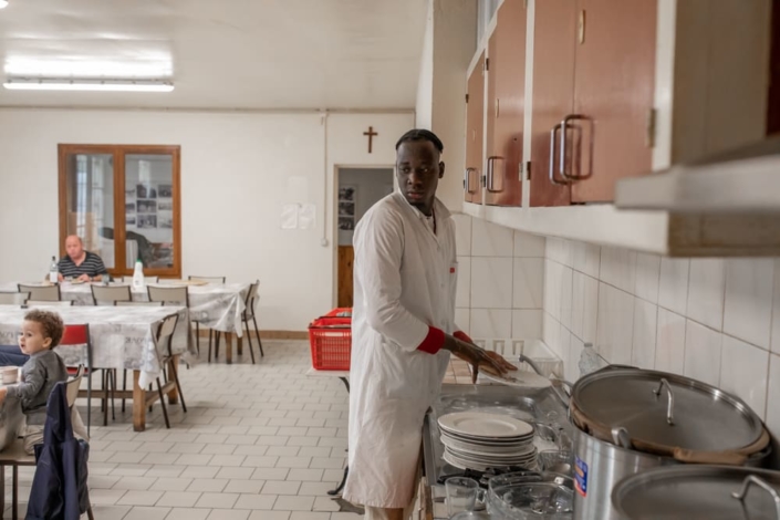 Un migrant fait la vaisselle dans un réfectoire.