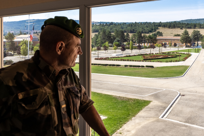 Un militaire regarde la place d'armes à travers une fenêtre.