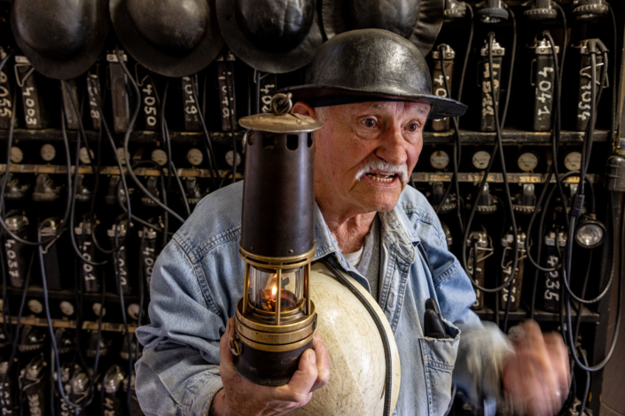 Portrait d'un mineur portant un casque et tenant une lampe à pétrole allumée à l'entrée d'une galerie