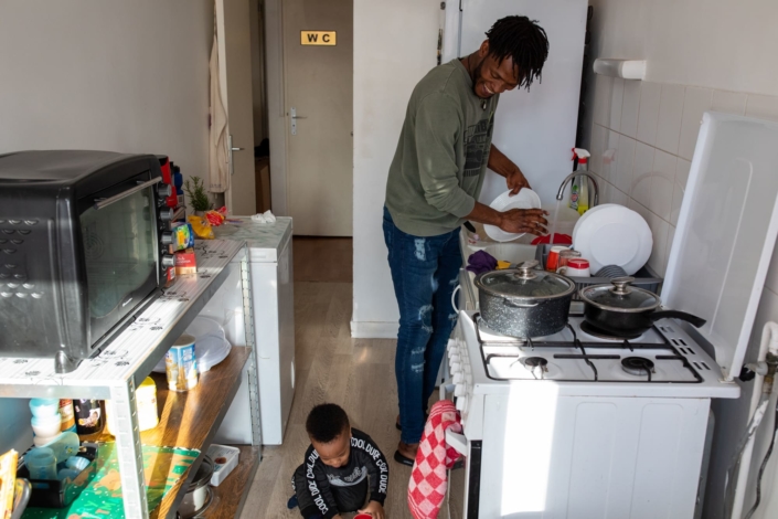 Un Africain fait la vaisselle en surveillant son enfant jouer