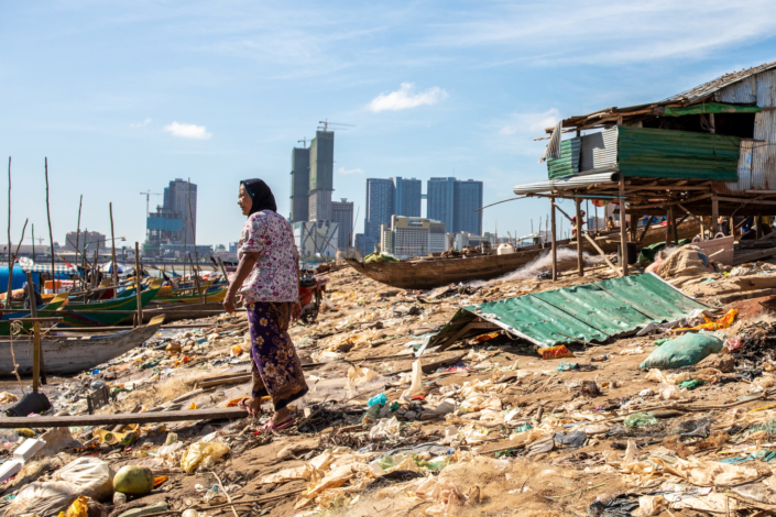 Une femme traverse un bidonville. Au fond les tours modernes de la ville de Phnom Penh