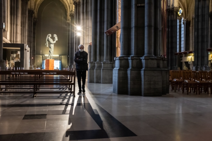 Un homme de face marche à contre jour dans un rai de lumière. Il se recueille dans une basilique.