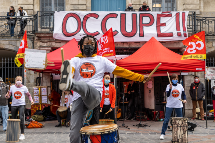 Artistes devant une banderole rouge "occupé" en arrière plan.