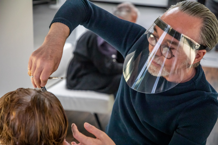 Le coiffeur porte une visière et coiffe sa cliente.