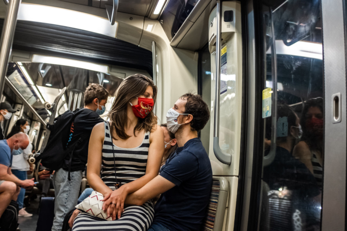 Un couple de touristes masques se regardant dans les yeux, dans le metro parisien
