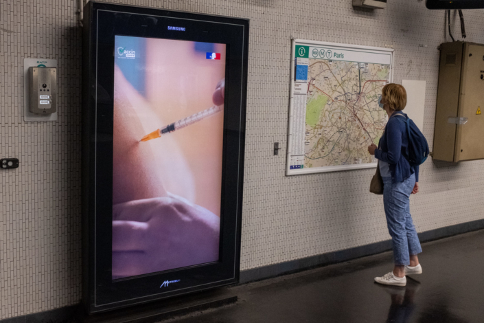 Dans le metro une passante regarde un plan a cote d'un grand panneau montrant une aiguille vacciner un bras