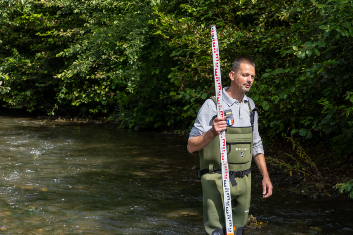 Un inspecteur de la police se tient debout dans la rivière pour mesurer la pente du lit. Vue sur ses insignes de la police .