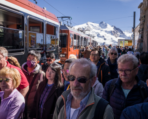 Une foule sur le quai de la gare longe un train . Montagnes en arrière plan