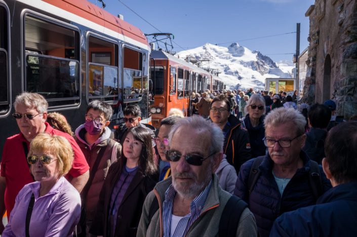 Une foule sur le quai de la gare longe un train . Montagnes en arrière plan